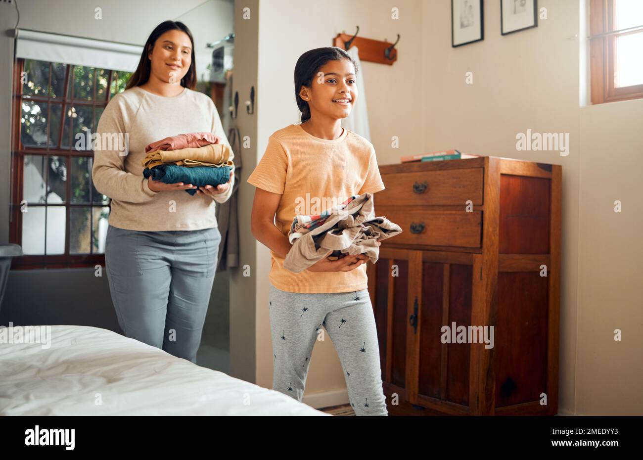 Petite fille, maman et aider avec la lessive pour les corvées, les vêtements ou le lavage plié avec le sourire à la maison. Enfant heureux marchant avec la mère portant propre Banque D'Images