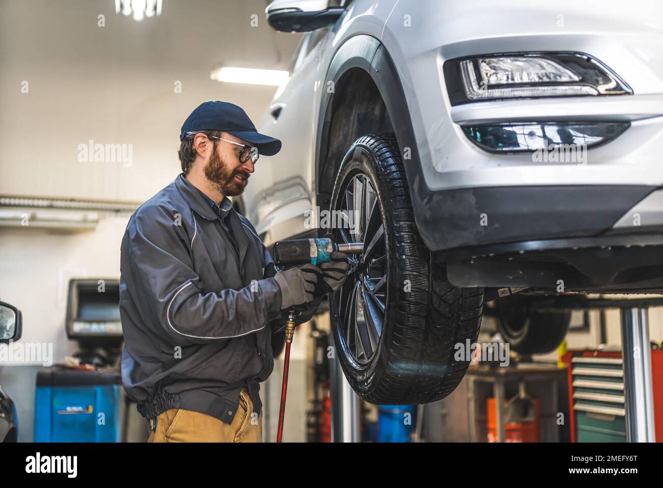 Le mécanicien qui change les pneus à l'aide d'une clé électrique est soulevé pour un processus régulier. Photo de haute qualité Banque D'Images