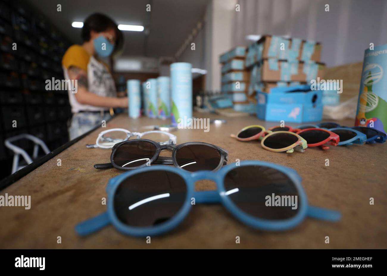 A Saju staffer packs glasses made from recycled plastic bottle tops to be mailed to customers, at the Saju company in Bogotá, Colombia, Tuesday, April 6, 2021. The company buys platic soda bottle tops that have been turned into small pellets by a recycling plant, melts down the material and injects it into molds to produce colorful frames. Dark lenses are then mounted on the frames, to make shades that are sold at Saju's stores for about $40 each. (AP Photo/Fernando Vergara) Banque D'Images