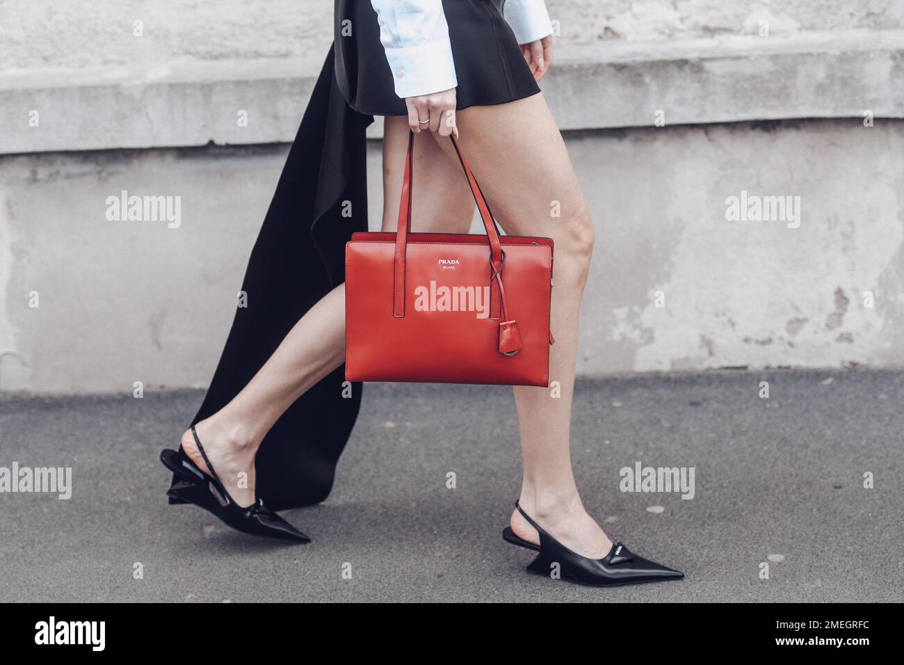 Milan, Italie - 24 février 2022: Femme en robe noire avec manches blanches portant des chaussures pointues inhabituelles marchant dans la rue avec sac à main rouge. Banque D'Images