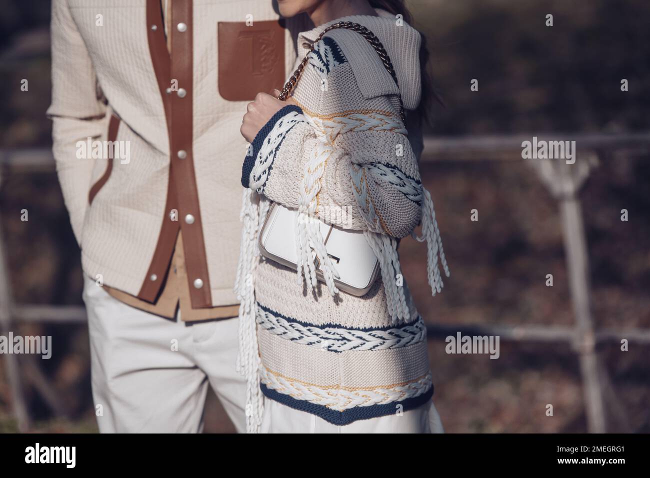 Milan, Italie - 24 février 2022: Homme en pantalon beige et surshirt matelassé avec poches en cuir marron marche avec femme en jupe et sweat tricoté Banque D'Images