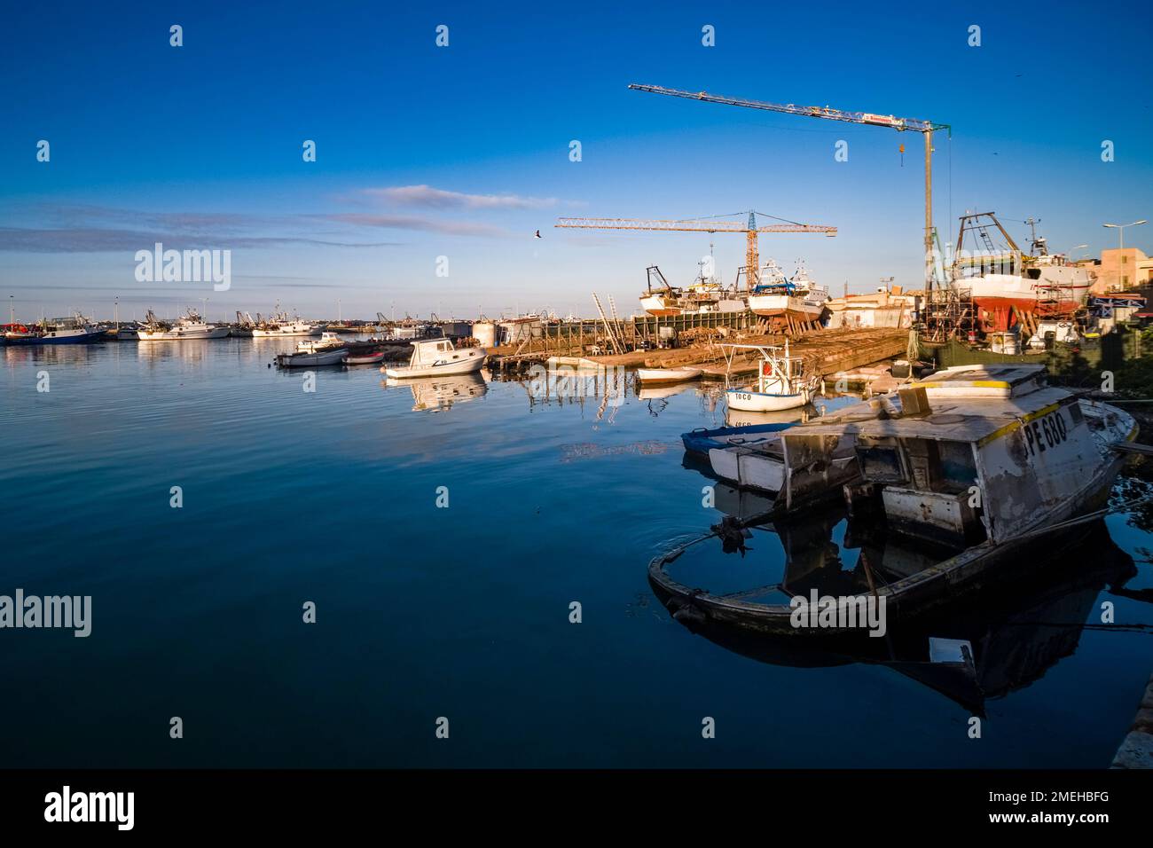 Docks, grues et bateaux de pêche, dont l'un est en contrebas, dans le port de Sciacca. Banque D'Images