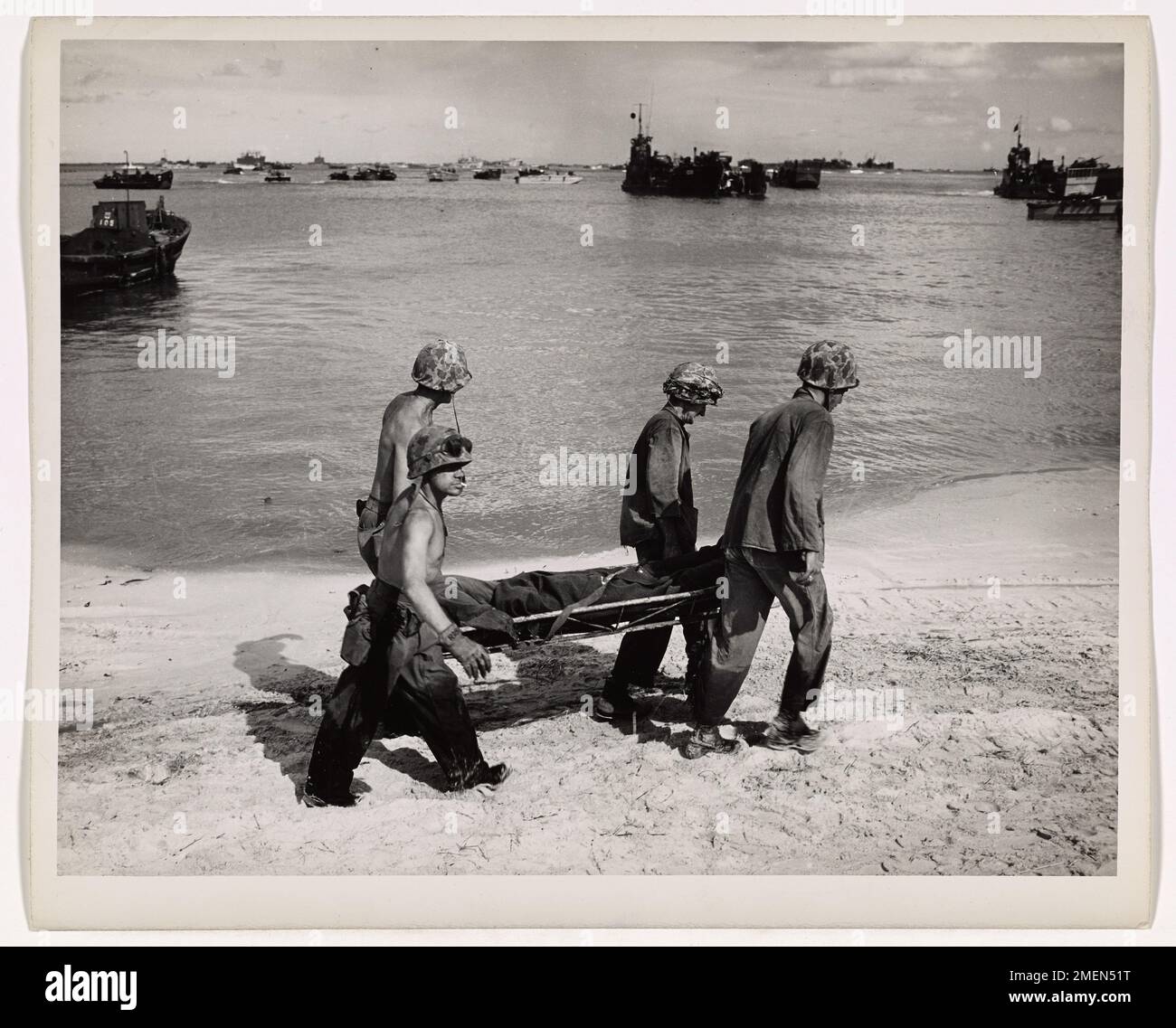 Quelques litières de retour. Un combattant américain blessé sort du carnage de Saipan. Quatre camarades portent une victime dans une portée le long de la plage jusqu'à une barge d'atterrissage qui l'emportera vers un LST assuré par la Garde côtière qui sert de navire-hôpital au large de l'île battue dans les Mariannes. Banque D'Images