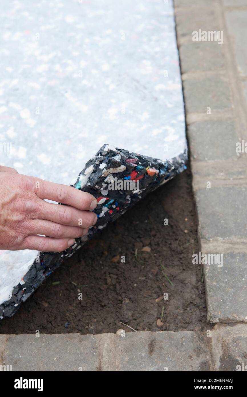 Pose d'une couche de matériau absorbant les chocs dans le jardin, comme base pour le gazon artificiel Banque D'Images