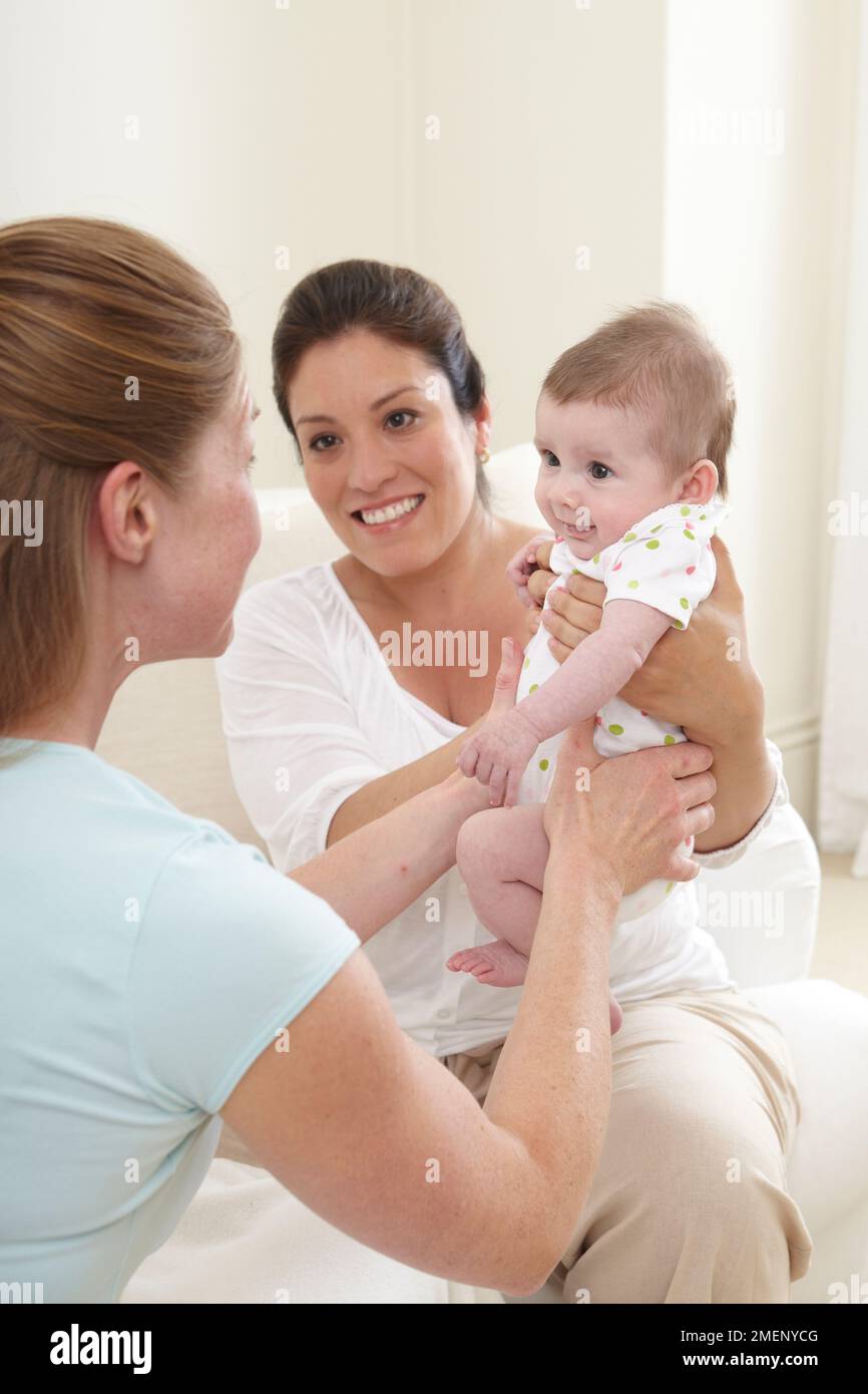 Mère souriante tenant bébé fille (3 mois) vers le haut pour l'ami Banque D'Images