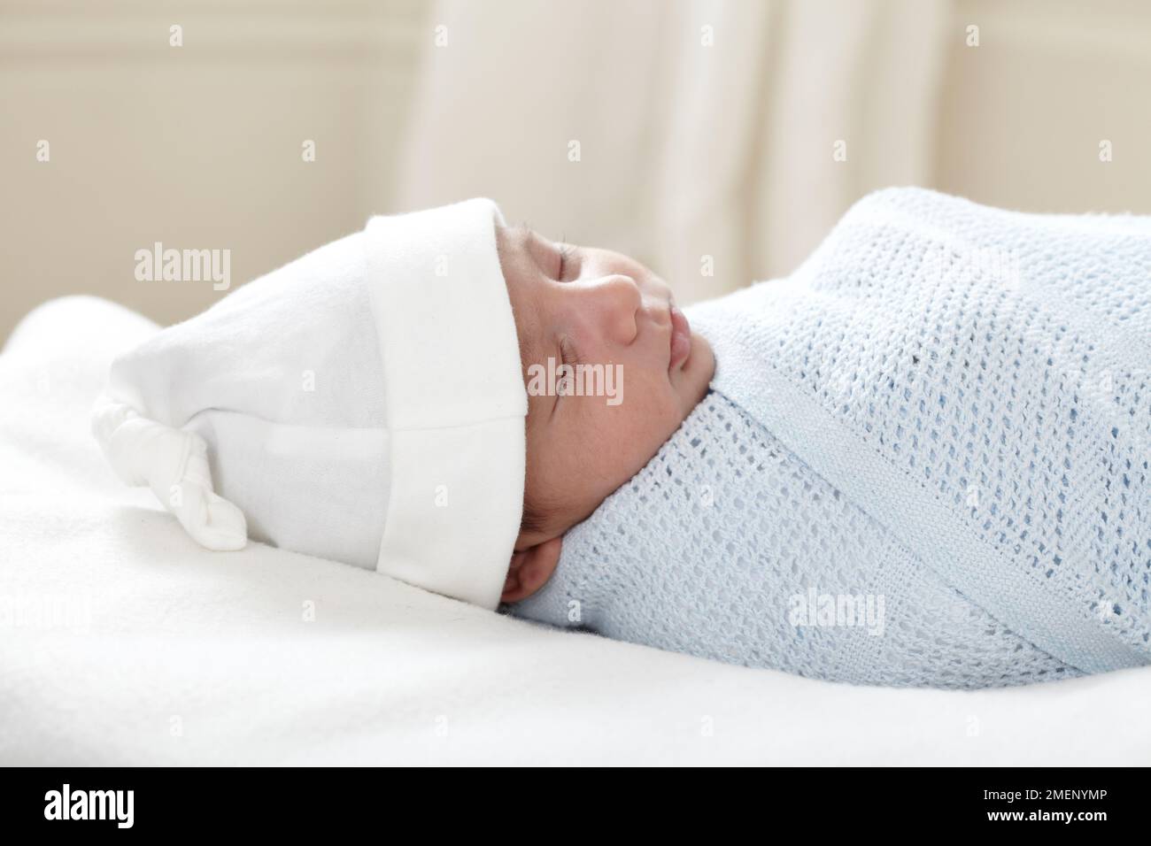 Bébé garçon endormi (3 semaines) enveloppé dans une couverture portant un chapeau, vue latérale Banque D'Images
