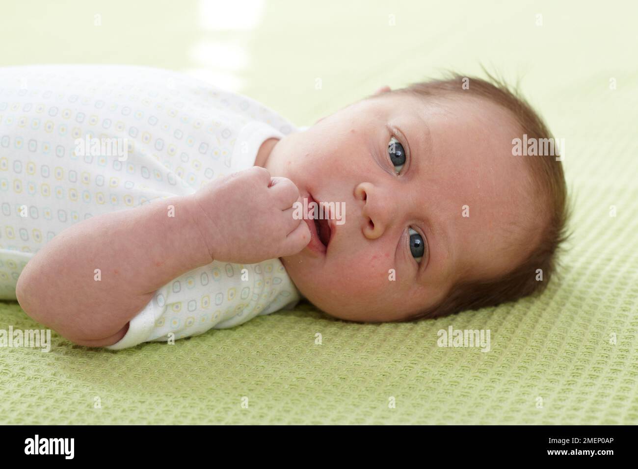 Bébé garçon (3 semaines) couché sur le dos sur une couverture verte, gros plan Banque D'Images