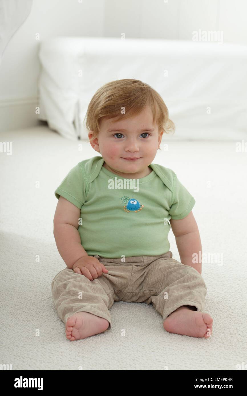 Bébé souriant (11,5 mois) assis sur la moquette, vue de face Banque D'Images