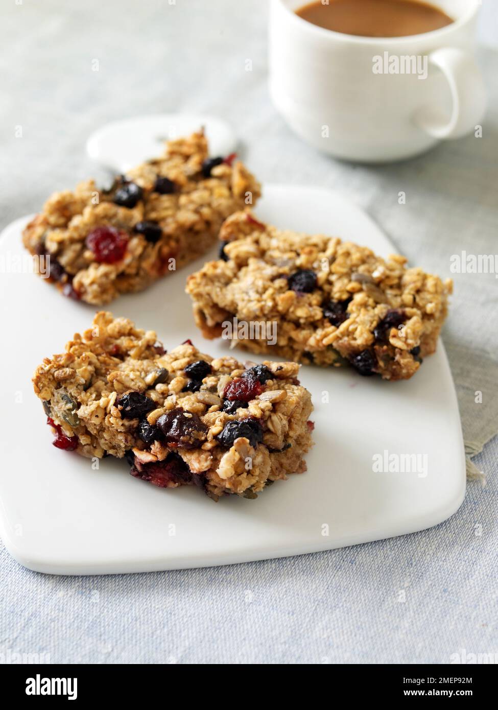 Trois barres de petit-déjeuner maison sans gluten, fruits et noix, sur planche à découper blanche, avec une tasse de café Banque D'Images