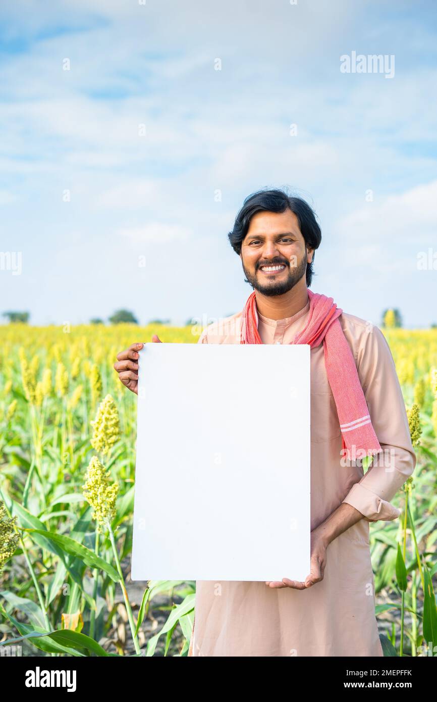 Plan vertical de jeunes agriculteurs indiens heureux tenant un panneau vide sur les terres agricoles - concept de publicité, de promotion et d'agriculture moderne Banque D'Images