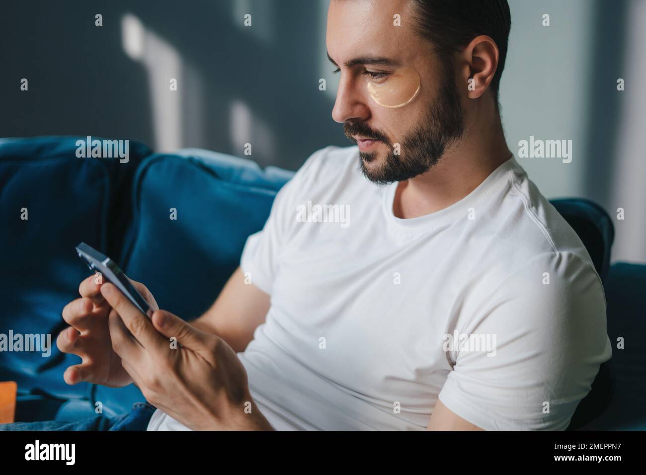Homme caucasien utilisant un smartphone tout en se reposant sur un canapé dans le salon. Utilisation des réseaux sociaux. Banque D'Images