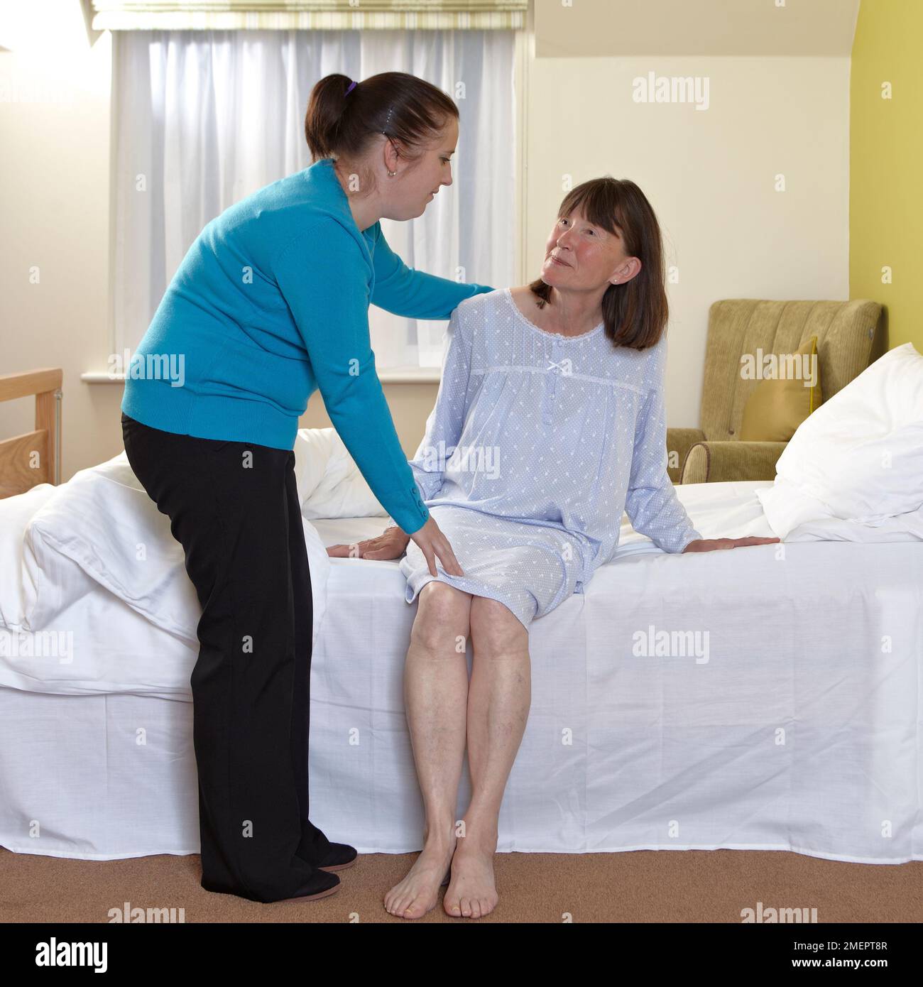 Aider une femme jusqu'à la position assise sur le bord du lit Banque D'Images