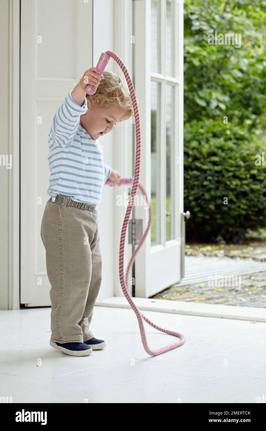 Garçon tenant une corde à sauter dans la porte, 2 ans 4 mois Banque D'Images