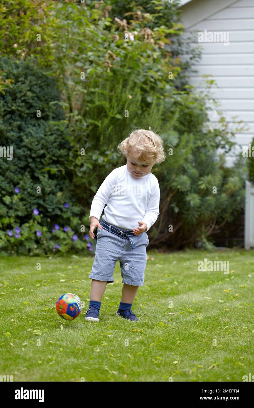 Un garçon frappe une balle dans un jardin, 2 ans 4 mois Banque D'Images