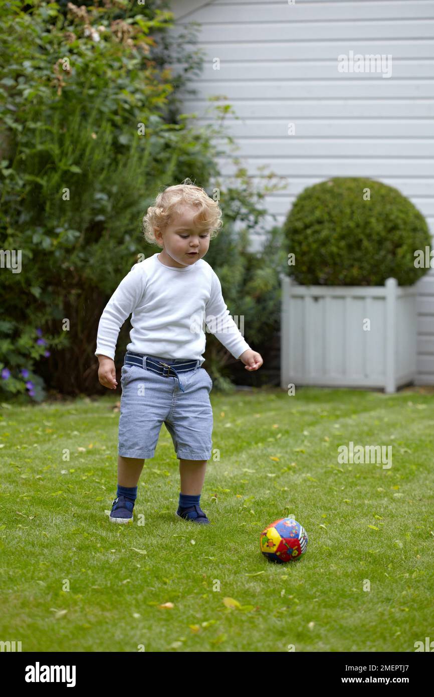 Garçon jouant au football dans le jardin, 2 ans 4 mois Banque D'Images