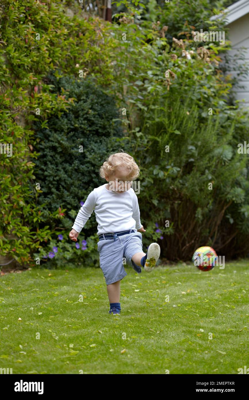 Garçon jouant au football dans le jardin, 2 ans 4 mois Banque D'Images