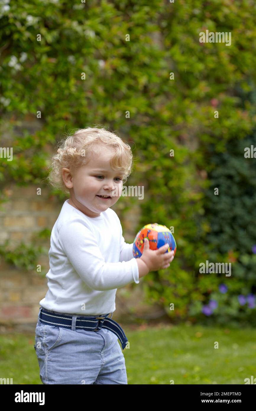 Garçon tenant un football dans le jardin, 2 ans 4 mois Banque D'Images