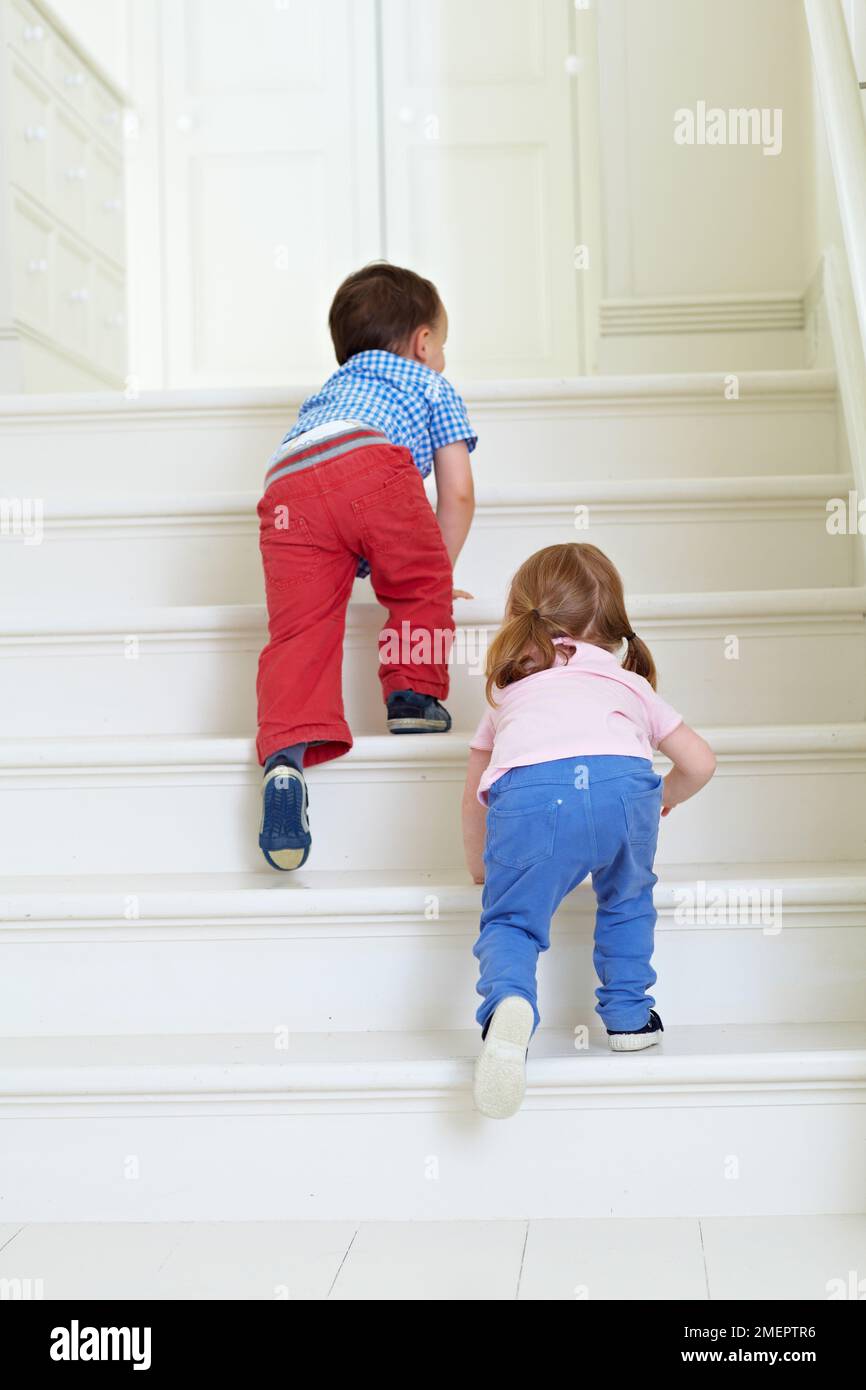 Garçon et fille grimpant les escaliers, 2 ans Banque D'Images