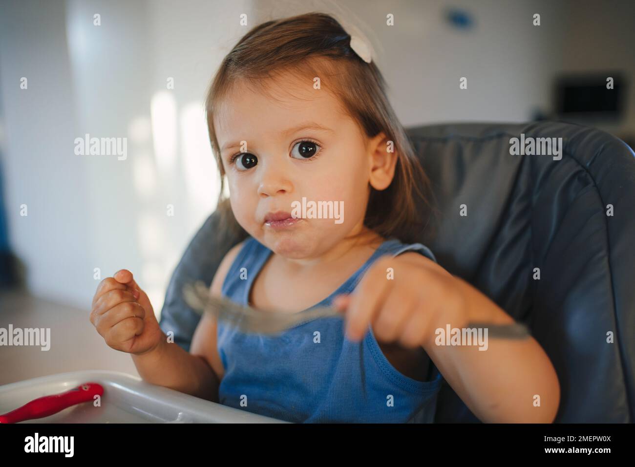 Petite fille de bébé de race blanche mangeant à la table seule à la maison dans la chambre, apprenant à tenir la fourchette et une saine alimentation. Auto-alimentation Banque D'Images
