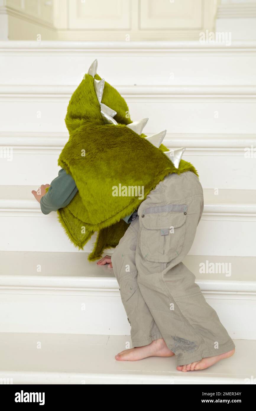Enfant dans un dinosaure vert ou un costume de dragon rampant dans les escaliers Banque D'Images