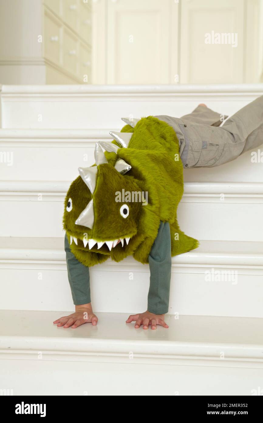 Enfant dans un dinosaure vert ou un costume de dragon grimpant dans les escaliers Banque D'Images