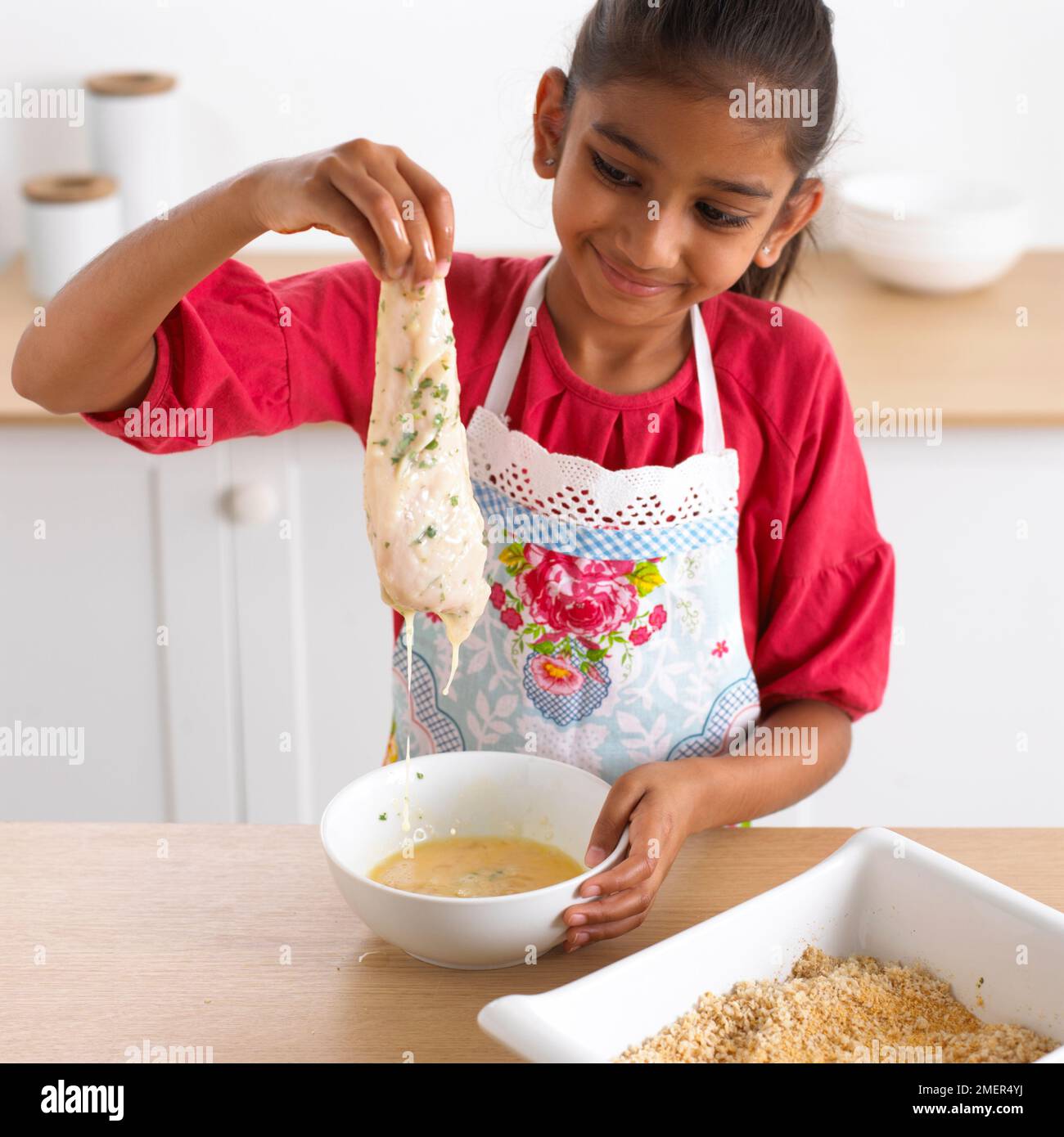 Fille trempant le poisson dans l'œuf avant la chapelure, 8 ans Banque D'Images