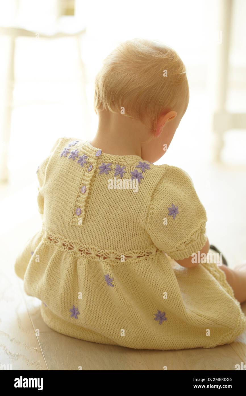 Bébé fille assise sur le sol portant une robe de Marguerite tricotée, 17 mois Banque D'Images