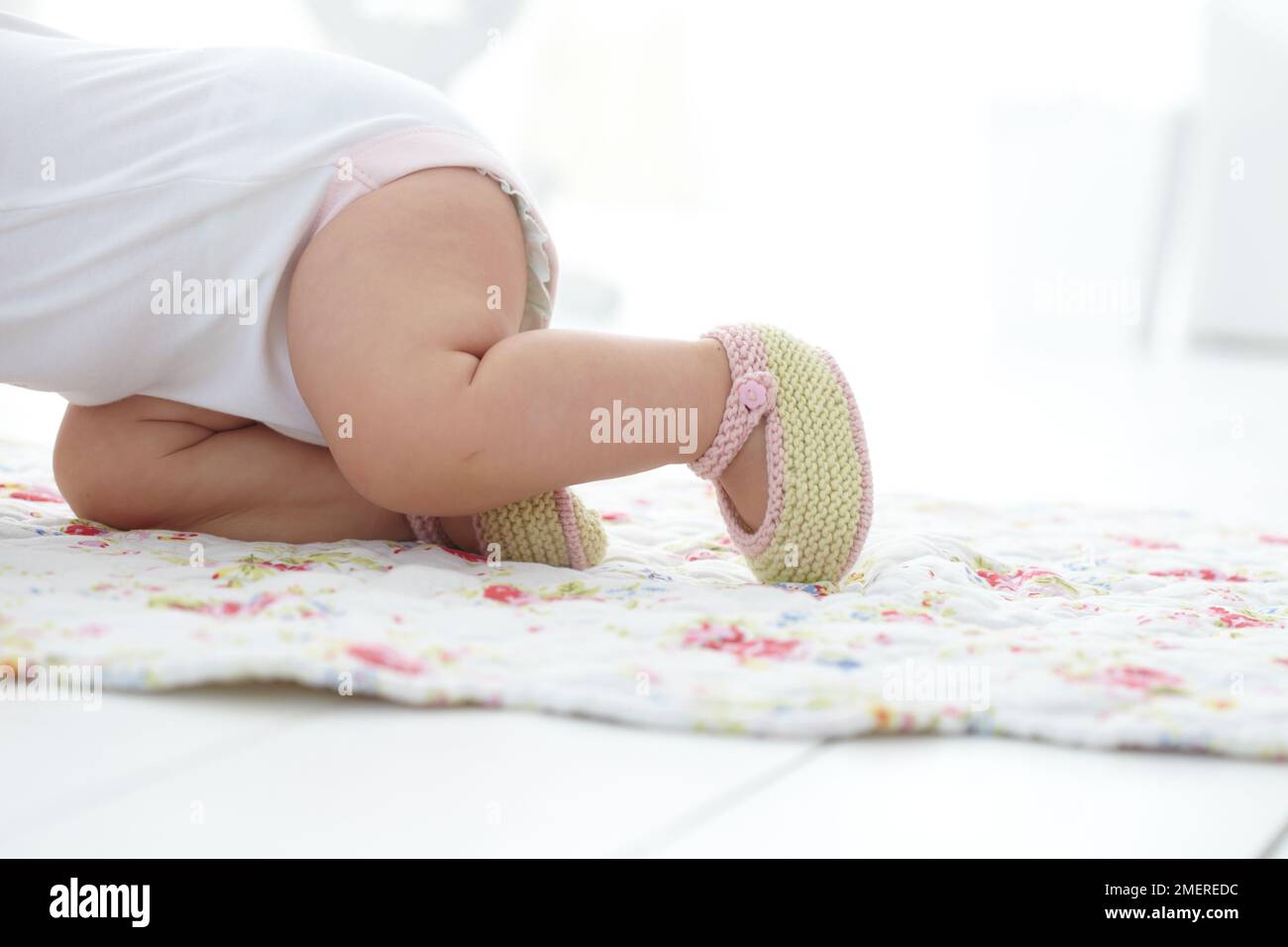 Bébé fille rampant portant des chaussons tricotés, 9 mois Banque D'Images