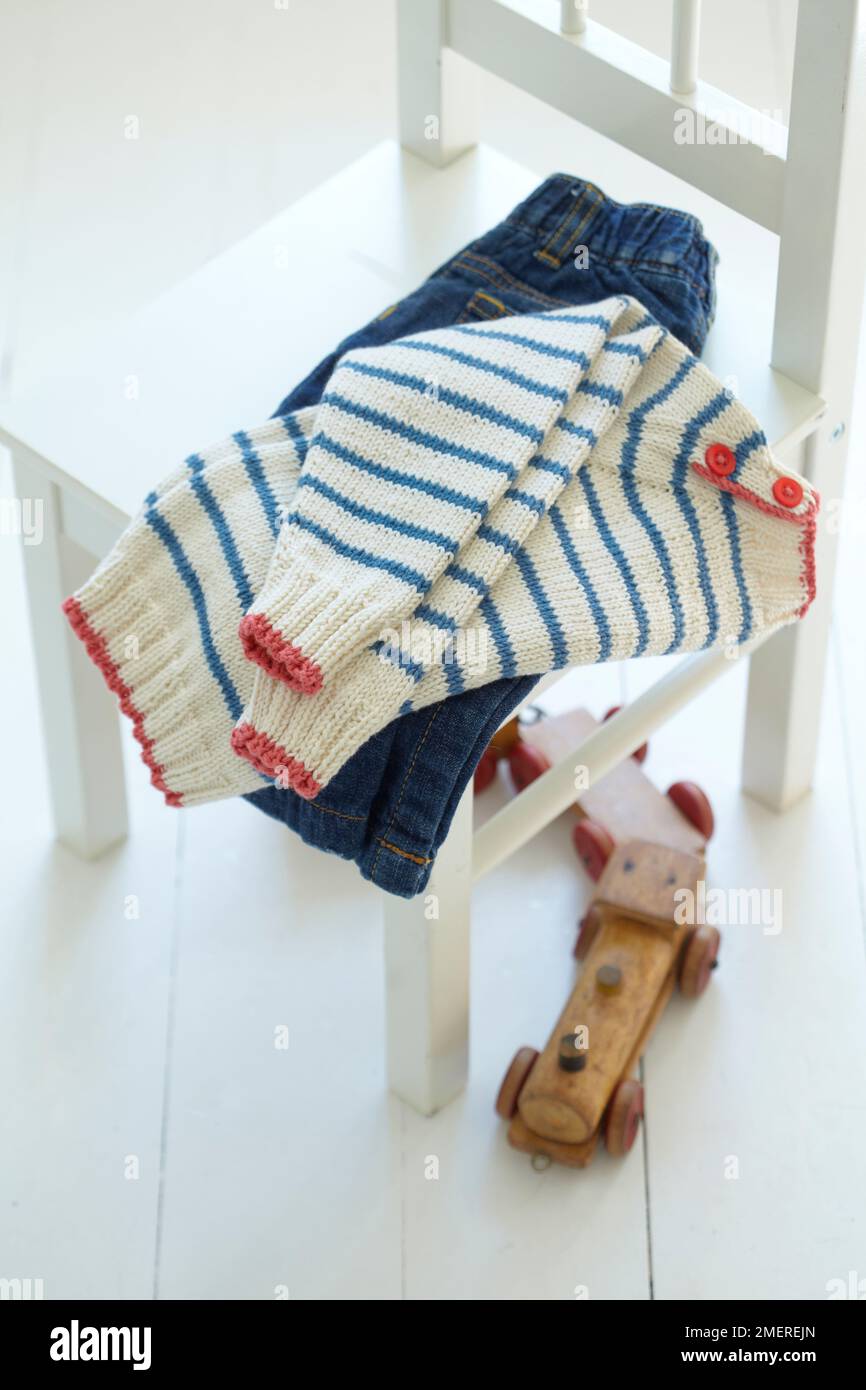 Vêtements pour enfants pliés sur une chaise, jeans et pull à rayures tricotées Banque D'Images