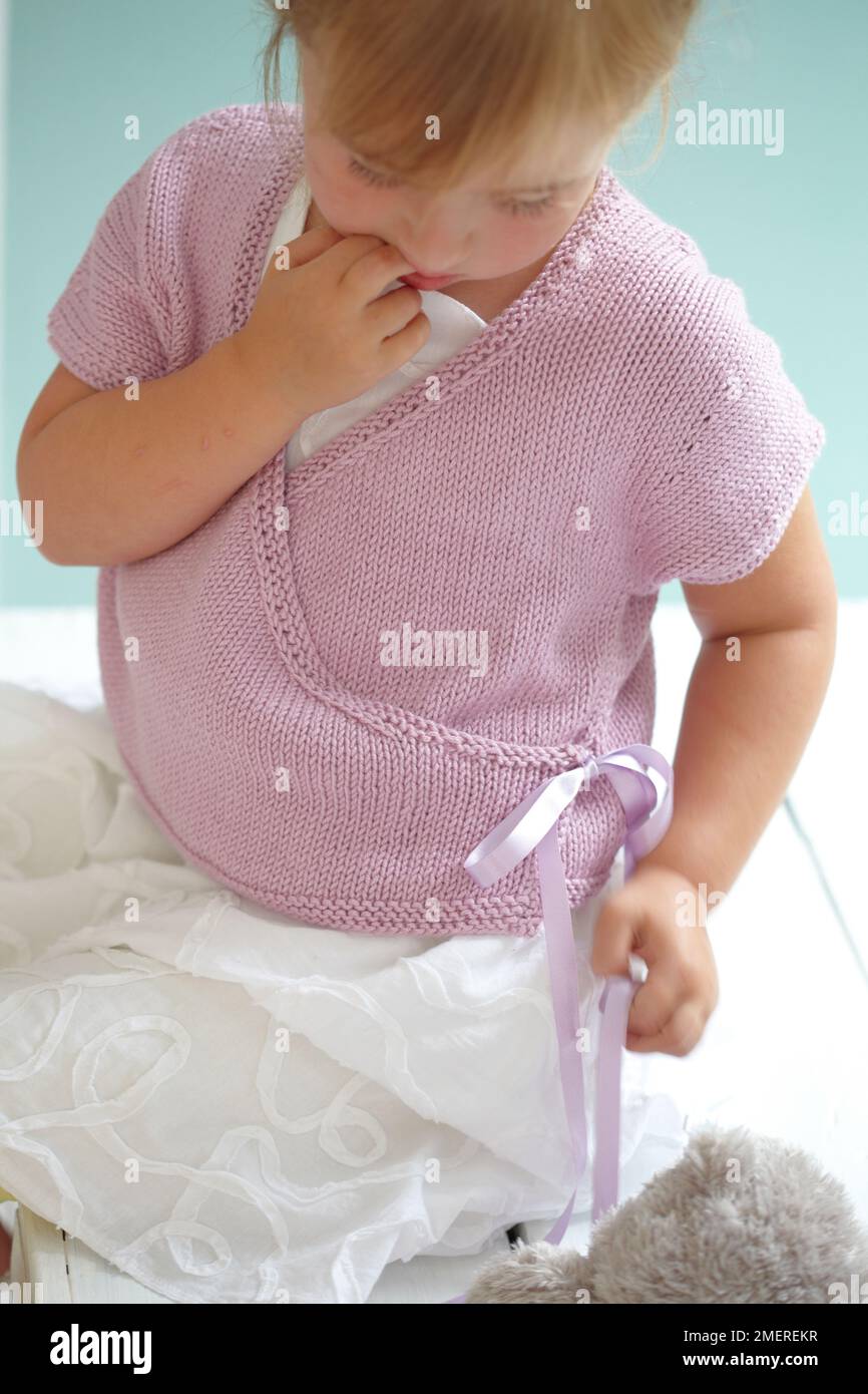 Fille assise portant une jupe blanche et un gilet portefeuille tricoté rose, 4 ans Banque D'Images