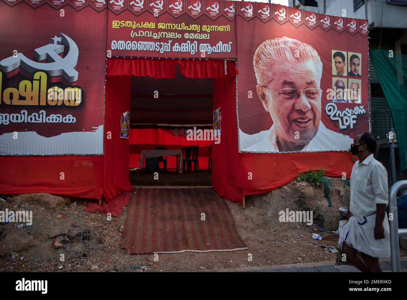 A man wearing a mask as a precaution against the coronavirus walks past an election campaign office of the left democratic front that displays a picture of chief minister Pinarayi Vijayan in Thiruvanathapuram, Kerala state, India, Saturday, April 3, 2021. The southern state goes to polls on April 6. (AP Photo/R S Iyer) Banque D'Images
