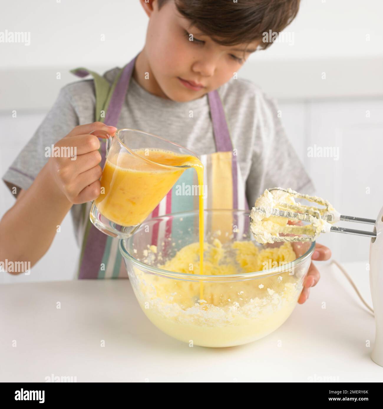 Garçon versant un pot d'œuf dans un bol de beurre et de sucre, 7 ans Banque D'Images