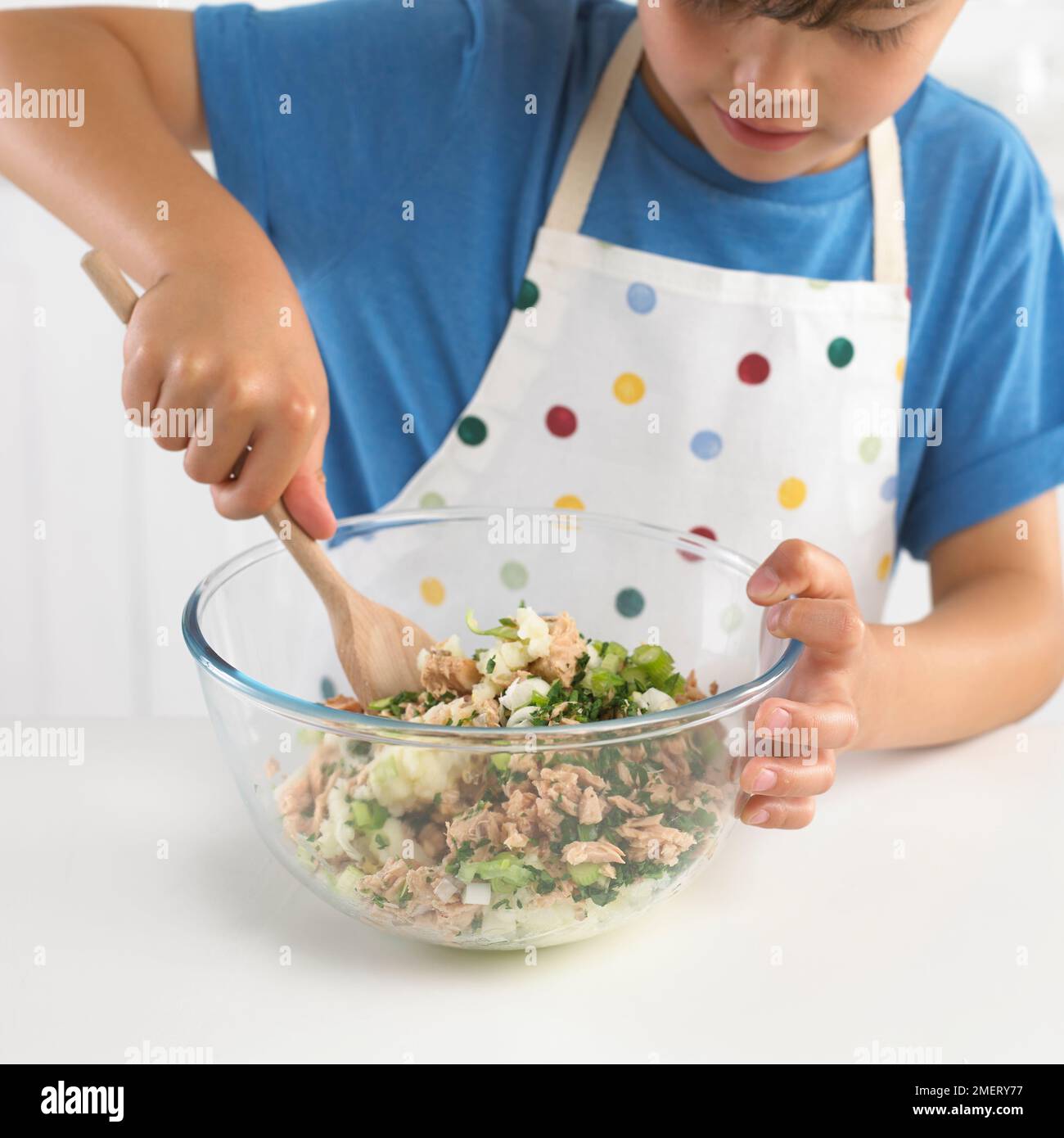 Faire des gâteaux de poisson, Boy mélangeant la pomme de terre, le poisson et l'oignon de printemps ensemble, 7 ans Banque D'Images