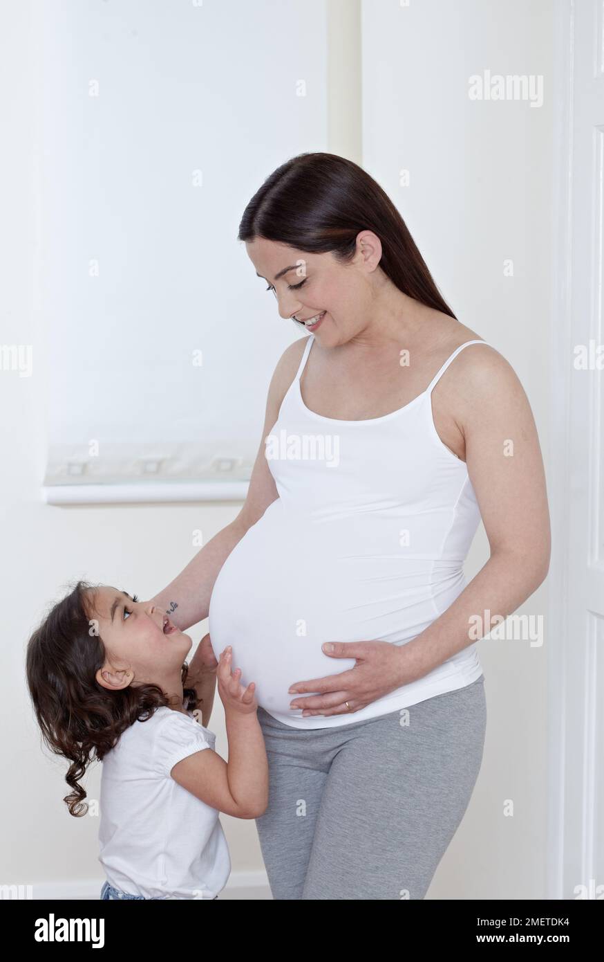 Fille (3,5 ans) touchant le ventre de sa mère enceinte Banque D'Images