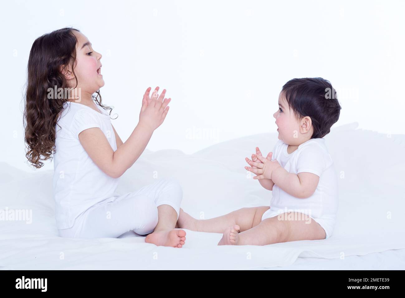Petite fille (40 semaines) et sa sœur aînée (3,5 ans) assise au lit, face à face, se claquant les mains Banque D'Images