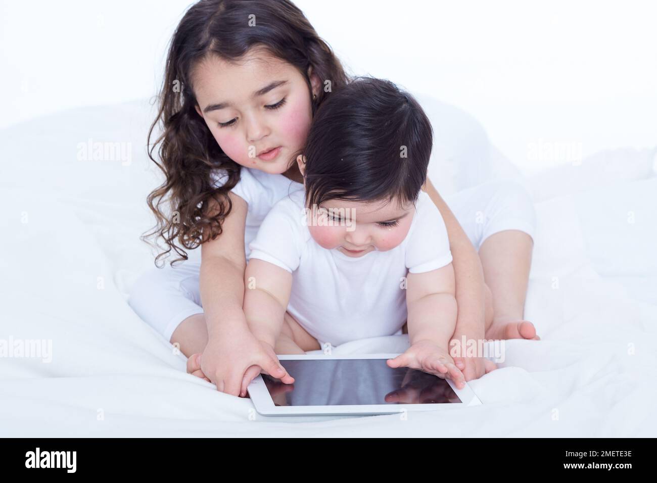 Bébé fille (40 semaines) et sa sœur aînée (3,5 ans) regardant un ordinateur tablette ensemble Banque D'Images