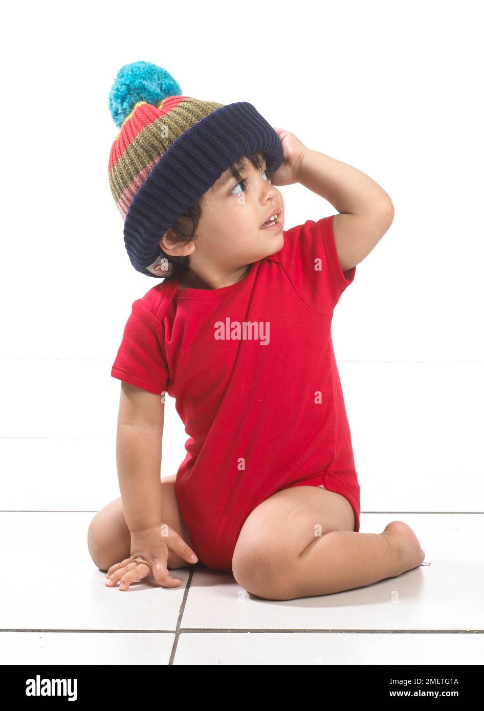 Garçon (16 mois) agenouillé au sol, portant une veste et un grand chapeau de galet tricoté Banque D'Images