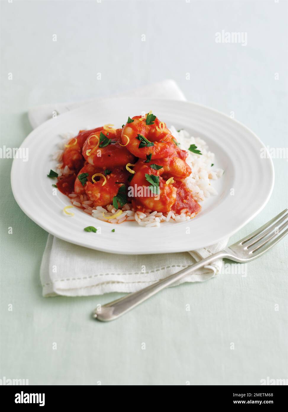 Crevettes à l'ail sauce tomate, garnies de persil haché et de zeste de citron, servies sur un lit de riz Banque D'Images