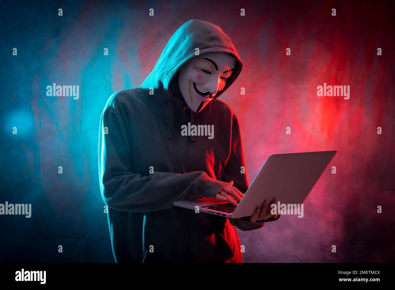 Hacker avec masque anonyme avec un ordinateur et avec un fond de fumée et LED colorée Banque D'Images