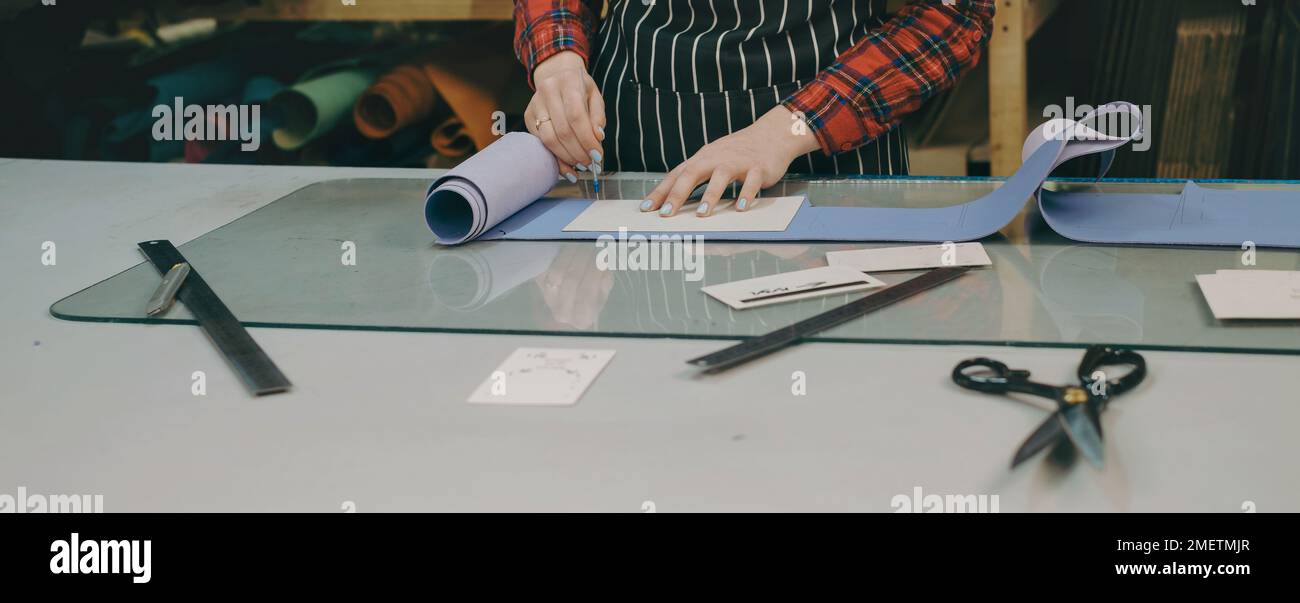 Processus de couture. Petites entreprises de fabrication de sacs en cuir et en toile. Femme coupe le cuir avec un couteau spécial sur son lieu de travail. Concept de personnalisation Banque D'Images