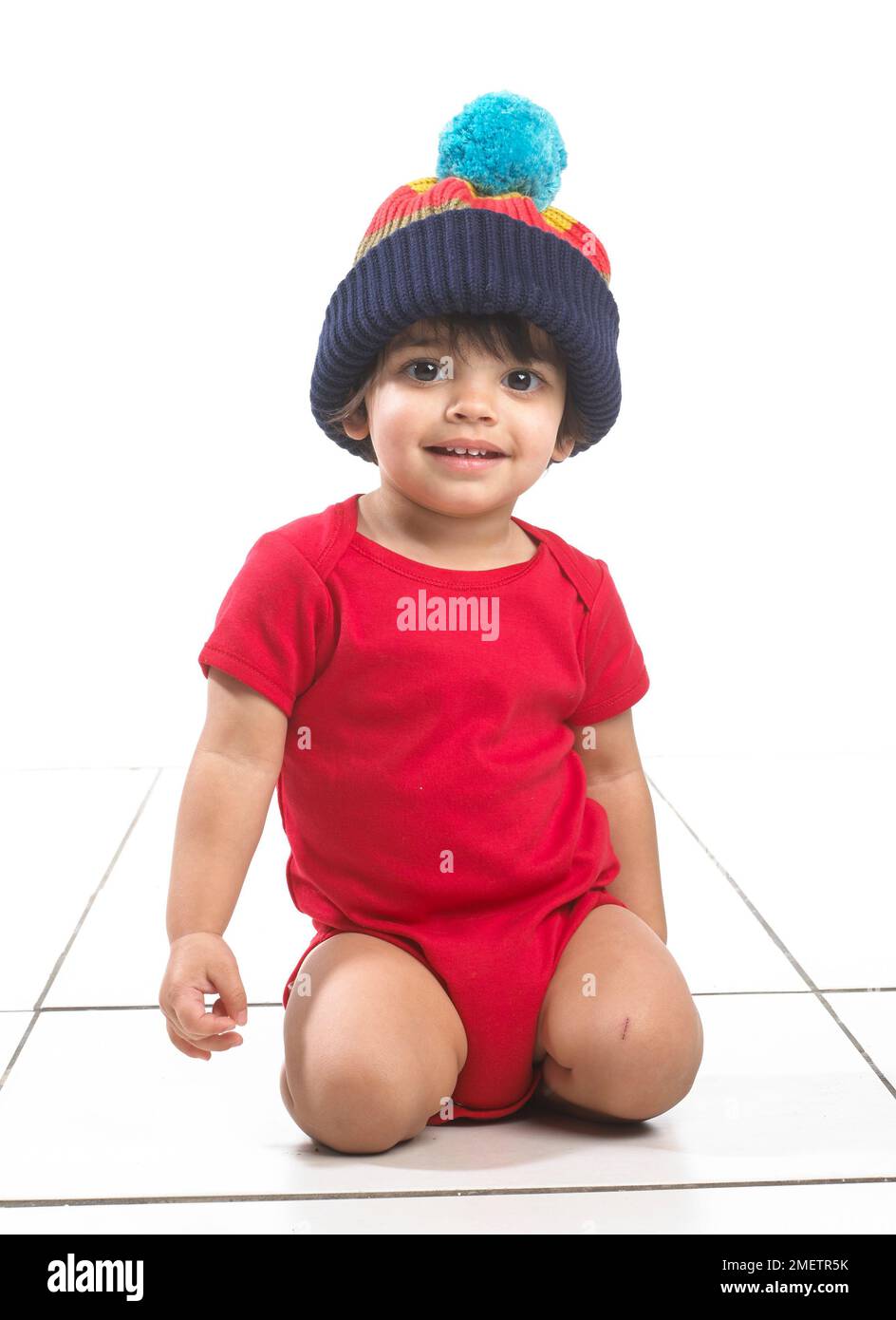Garçon (16 mois) agenouillé au sol, portant une veste et un grand chapeau de galet tricoté Banque D'Images
