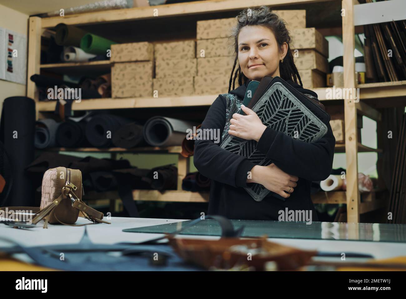 Des étuis en cuir écologique sur mesure pour ordinateur portable. Femme designer posant avec un produit textile en cuir écologique à son atelier. Concept de production artisanale Banque D'Images