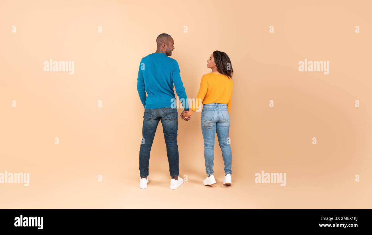 Pleine longueur d'homme noir et de femme debout avec leur dos à la caméra, regardant les uns les autres et tenant les mains Banque D'Images