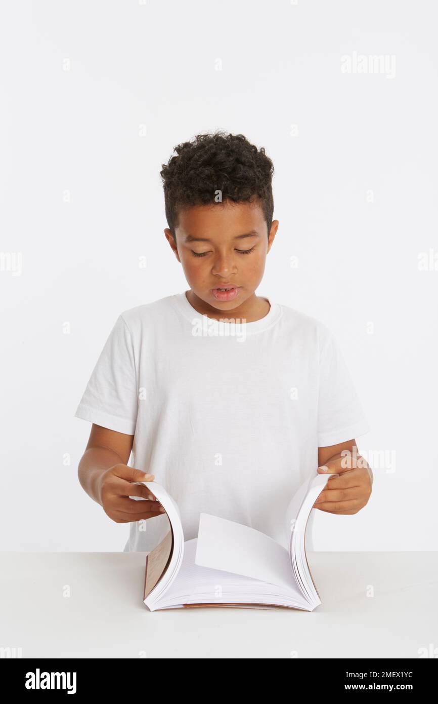 Enfant regardant les pages à l'intérieur de deux blocs-notes dans le cadre d'un test de friction. Modèle 8 ans. Banque D'Images