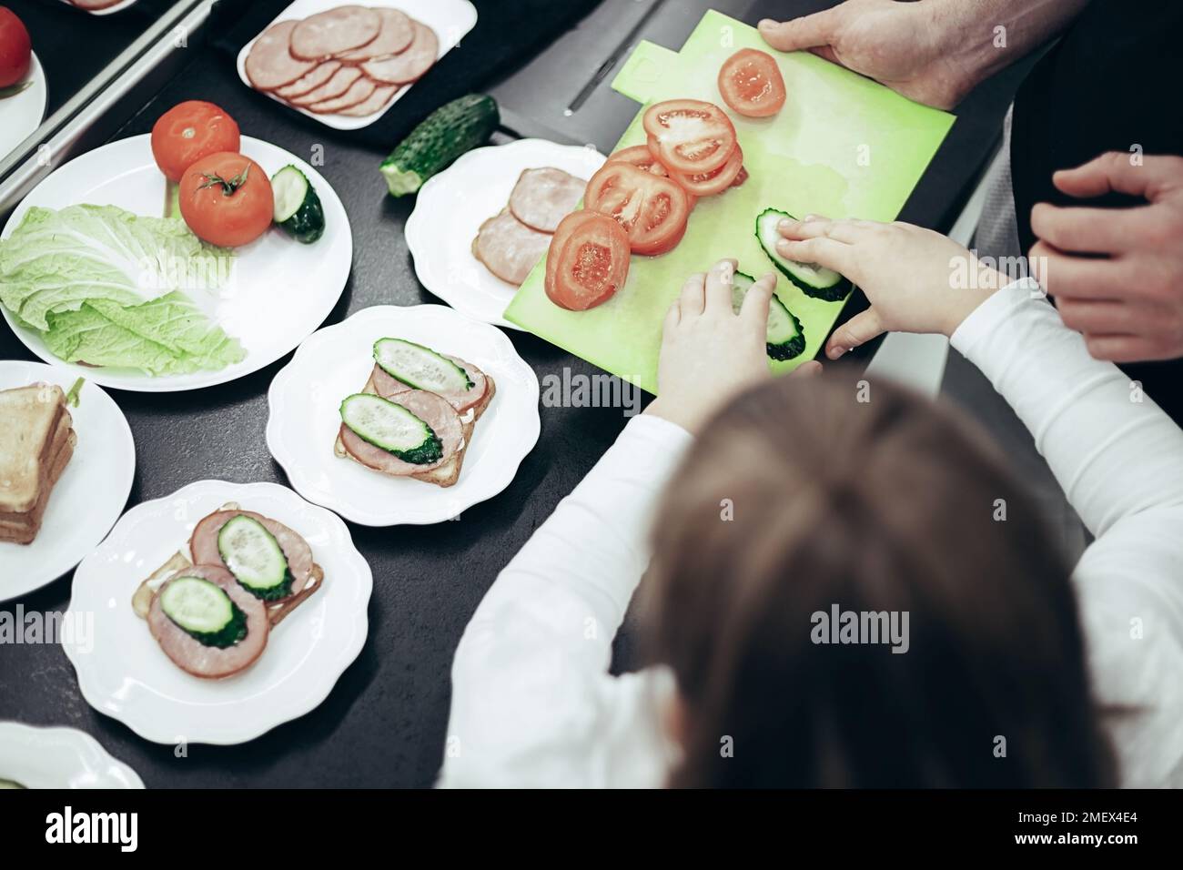Vue de dessus du père et de la fille cuisine petit déjeuner. Sandwiches avec légumes, bacon et pain sur table sombre Banque D'Images