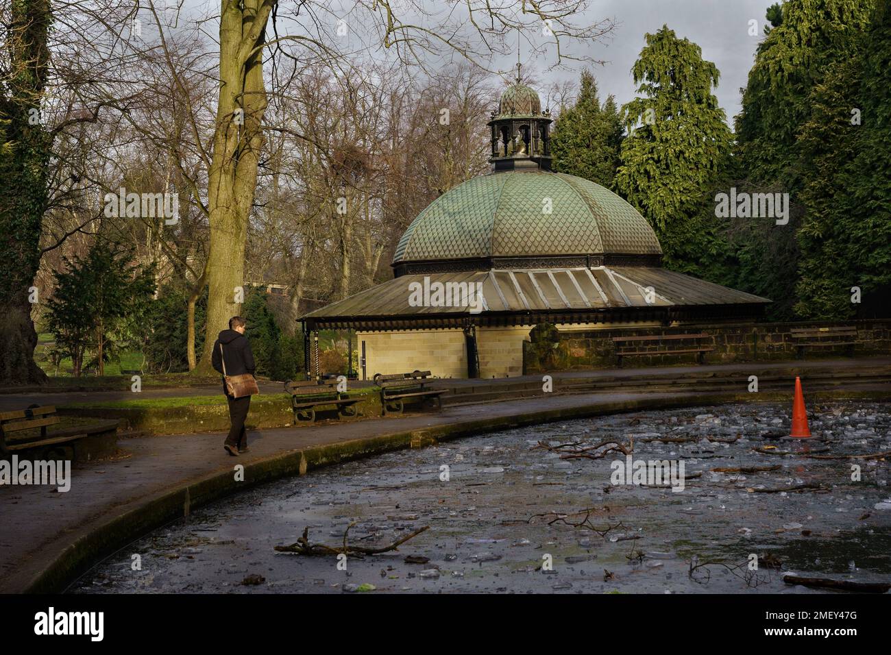 À Harrogate, au Royaume-Uni, un homme seul marche à côté d'un étang de canotage gelé près du Magnesia Well Cafe, une attraction touristique populaire. Banque D'Images