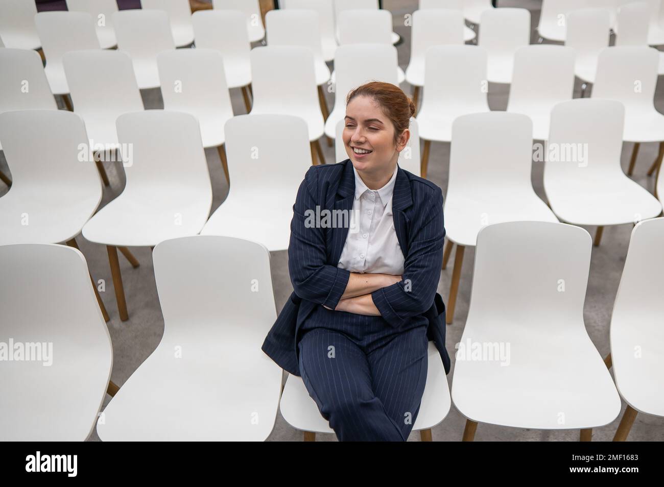 Une femme d'affaires caucasienne aux cheveux rouges est assise au premier rang dans une salle de conférence vide. Banque D'Images Une femme d'affaires caucasienne aux cheveux rouges est assise au premier rang dans une salle de conférence vide. Banque D'Images