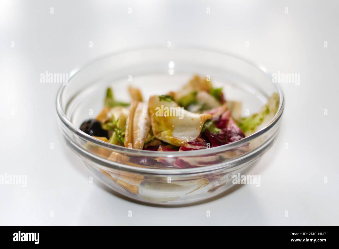 Permet de déconcentrer le bol en verre avec une salade sur fond blanc. Différentes feuilles de légumes à feuilles, verger, épinards, arugula, en salade. Salade au fromage. Banque D'Images