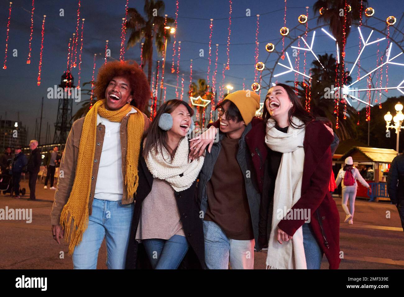 Groupe d'amis qui marchent dans le parc d'attractions la nuit avec leurs bras l'un autour de l'autre. Banque D'Images