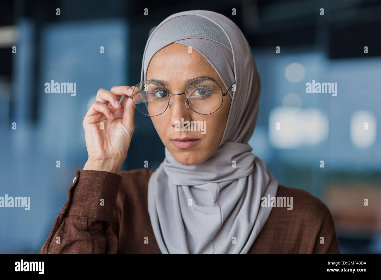 Gros plan. Portrait de la jeune belle femme arabe dans le hijab. Il regarde avec confiance dans l'appareil photo, soutient ses lunettes avec sa main. Banque D'Images